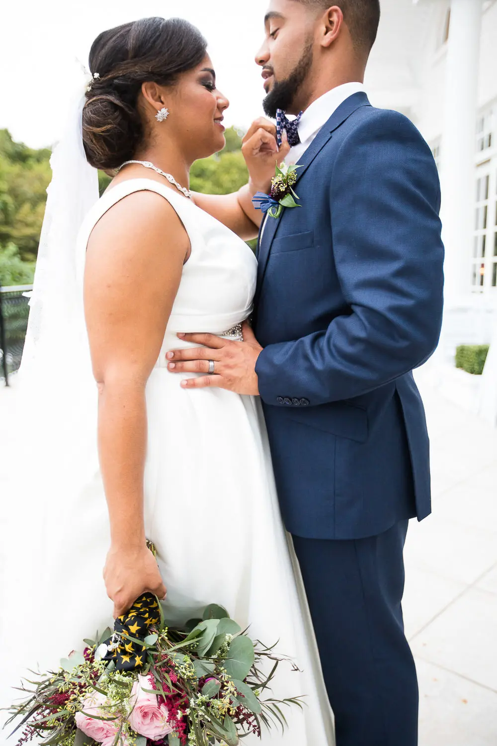 Bride and groom in a close embrace, bride adjusting groom's bow tie.